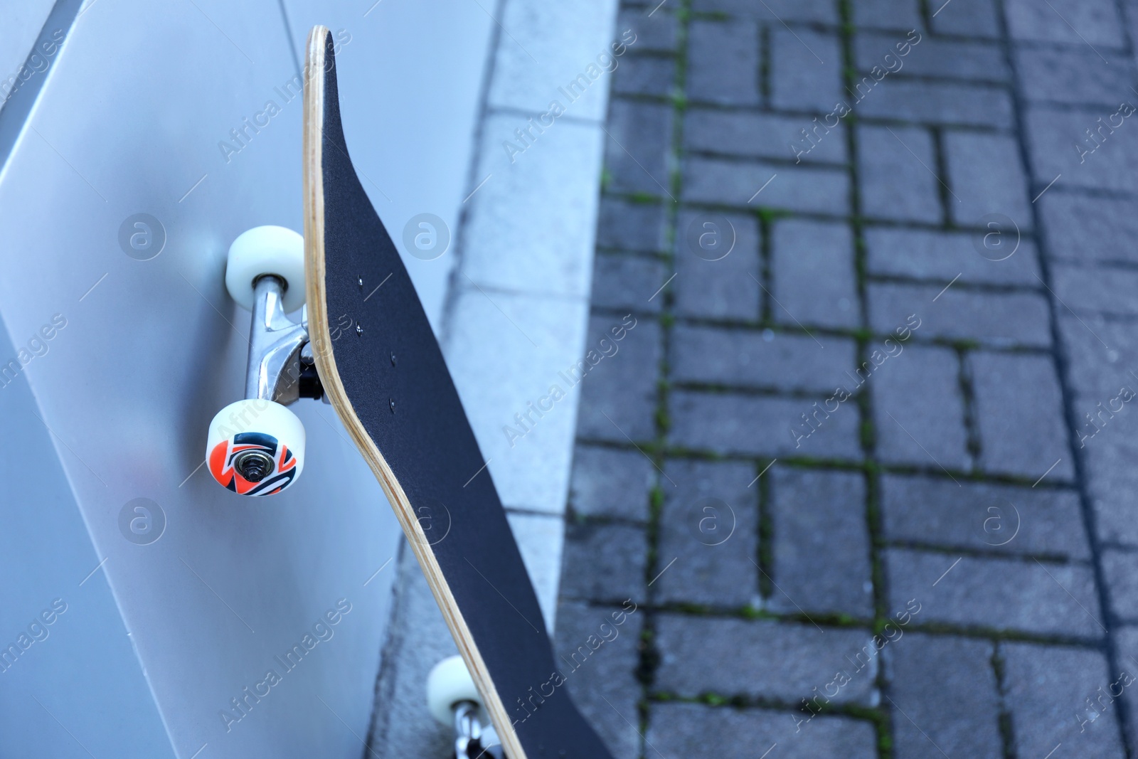 Photo of One modern skateboard near light wall outdoors, closeup. Space for text