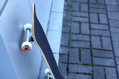 Photo of One modern skateboard near light wall outdoors, closeup. Space for text