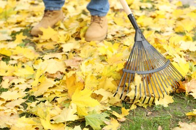 Photo of Man gathering fallen leaves with fan rake outdoors, closeup