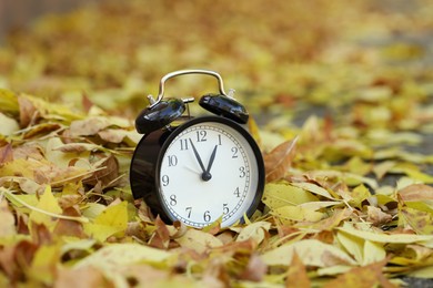 Photo of Autumn time. Alarm clock on fallen leaves, closeup