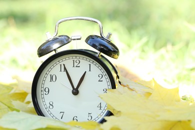 Photo of Autumn time. Alarm clock among fallen leaves, closeup