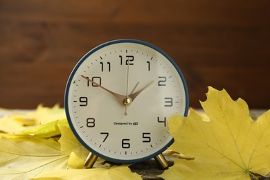 Photo of Autumn time. Alarm clock and leaves on wooden table, closeup