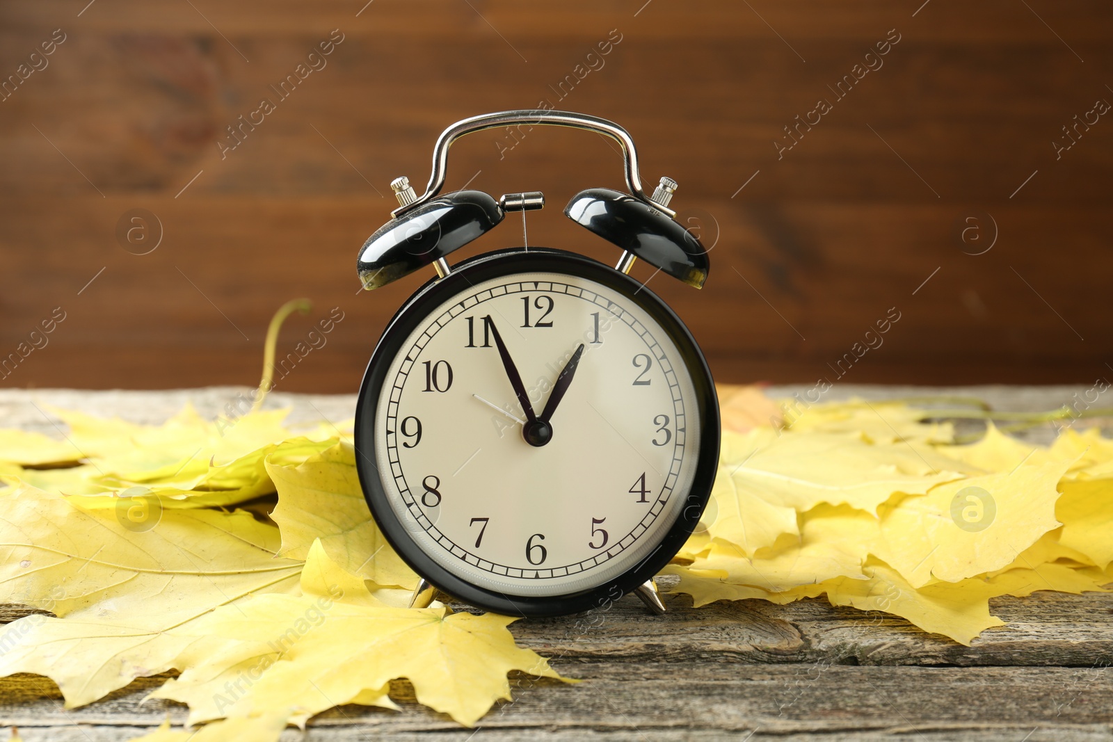 Photo of Autumn time. Alarm clock and leaves on wooden table, closeup