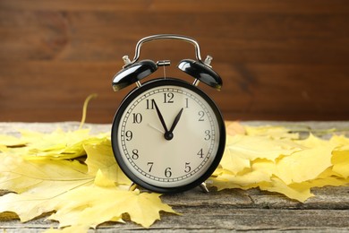 Photo of Autumn time. Alarm clock and leaves on wooden table, closeup