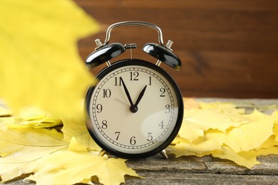 Autumn time. Alarm clock and leaves on wooden table, closeup