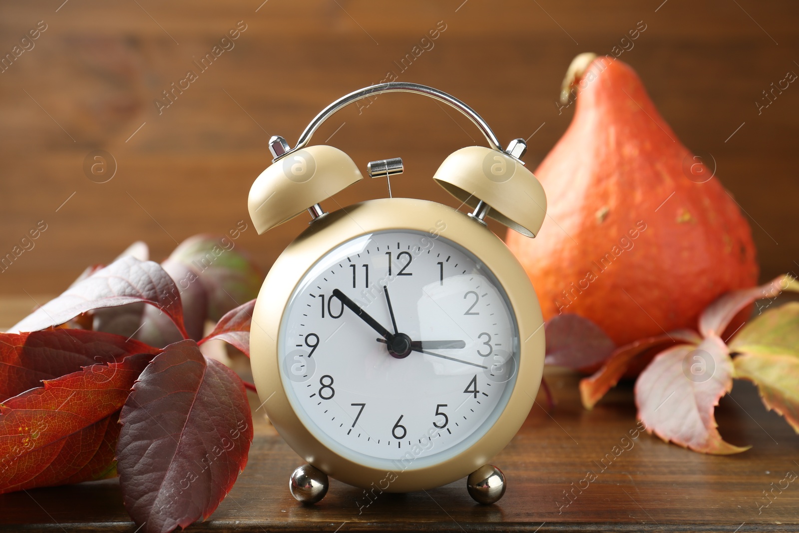 Photo of Autumn time. Alarm clock among leaves on wooden table, closeup