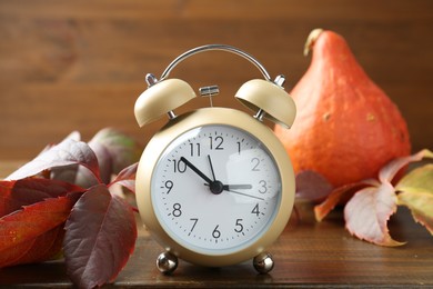 Photo of Autumn time. Alarm clock among leaves on wooden table, closeup