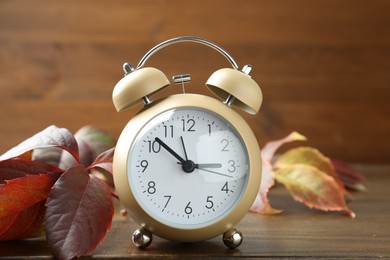 Autumn time. Alarm clock among leaves on wooden table, closeup