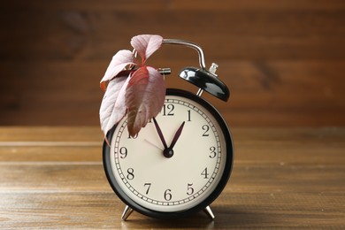 Photo of Autumn time. Alarm clock and leaves on wooden table, closeup