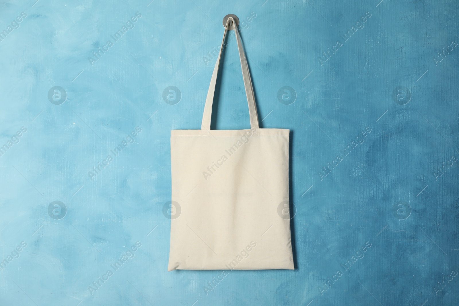 Photo of Eco bag hanging on light blue wall. Mockup for design