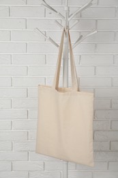 Eco bag hanging on clothing rack near white brick wall. Mockup for design