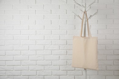 Photo of Eco bag hanging on clothing rack near white brick wall. Mockup for design