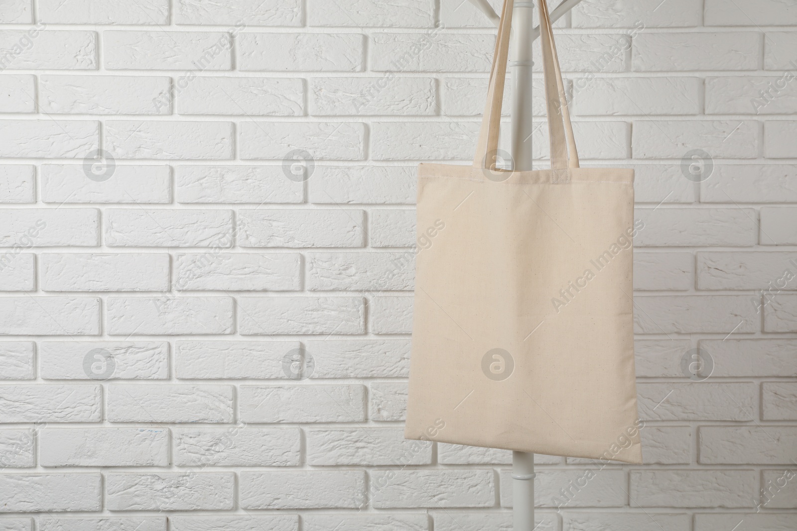 Photo of Eco bag hanging on clothing rack near white brick wall. Mockup for design