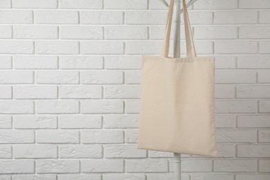 Eco bag hanging on clothing rack near white brick wall. Mockup for design