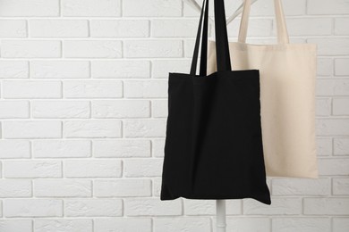 Photo of Eco bags hanging on clothing rack near white brick wall. Mockup for design