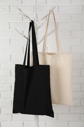 Photo of Eco bags hanging on clothing rack near white brick wall. Mockup for design