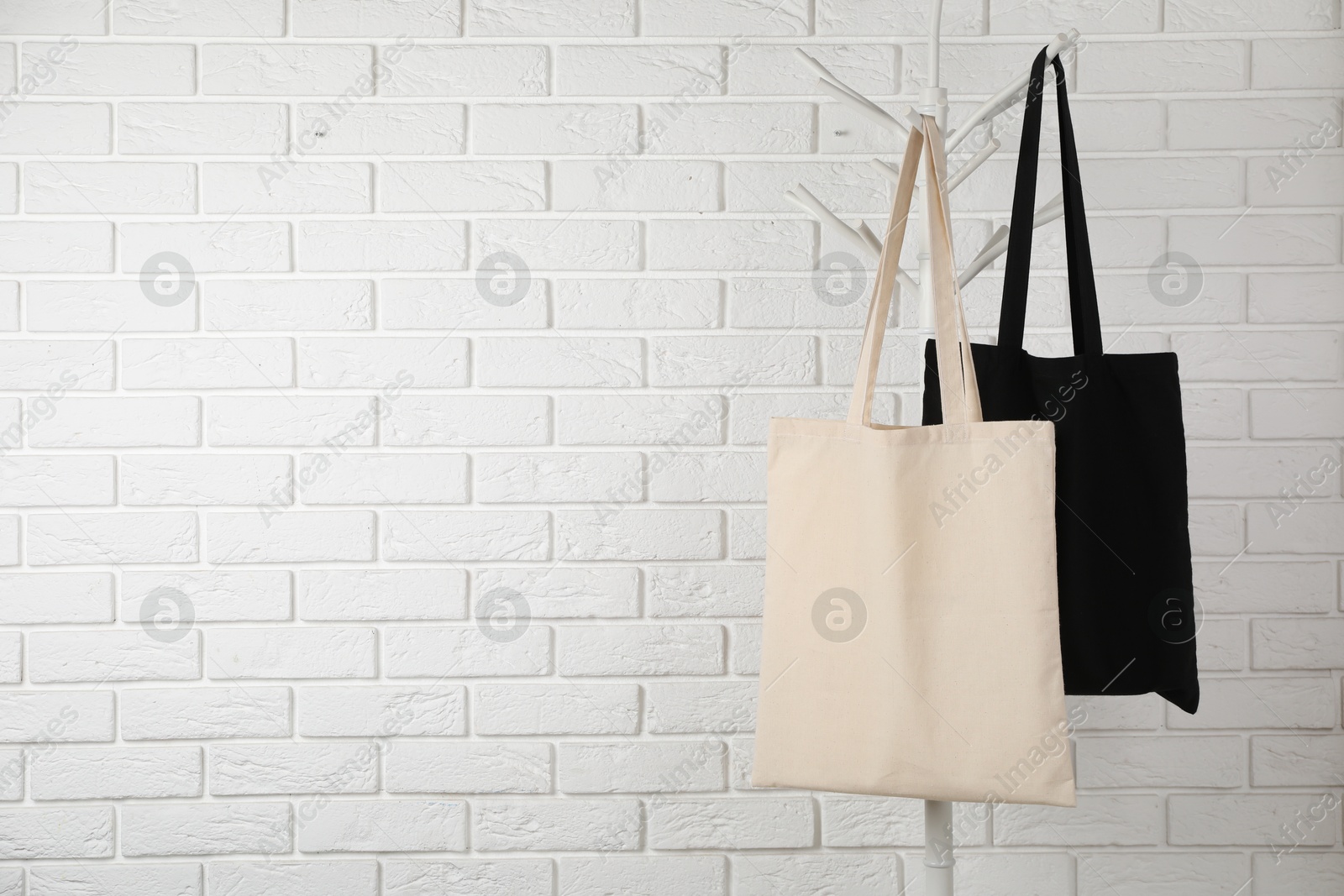 Photo of Eco bags hanging on clothing rack near white brick wall. Mockup for design