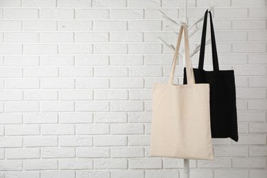 Eco bags hanging on clothing rack near white brick wall. Mockup for design