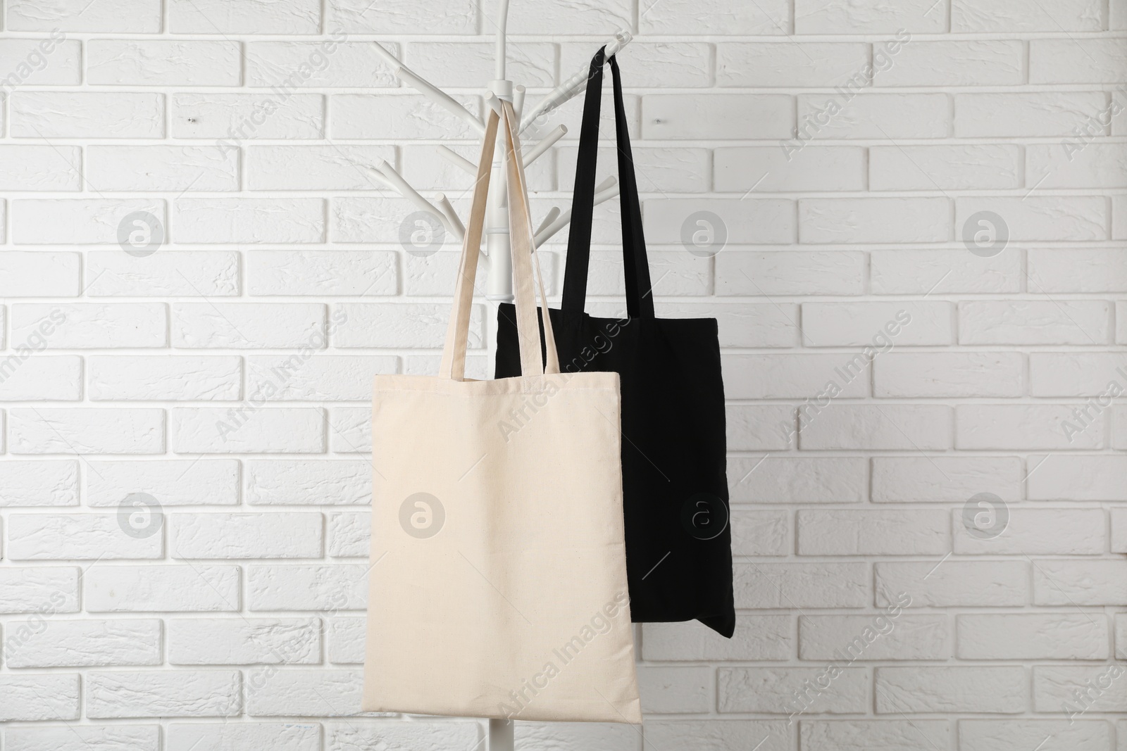 Photo of Eco bags hanging on clothing rack near white brick wall. Mockup for design