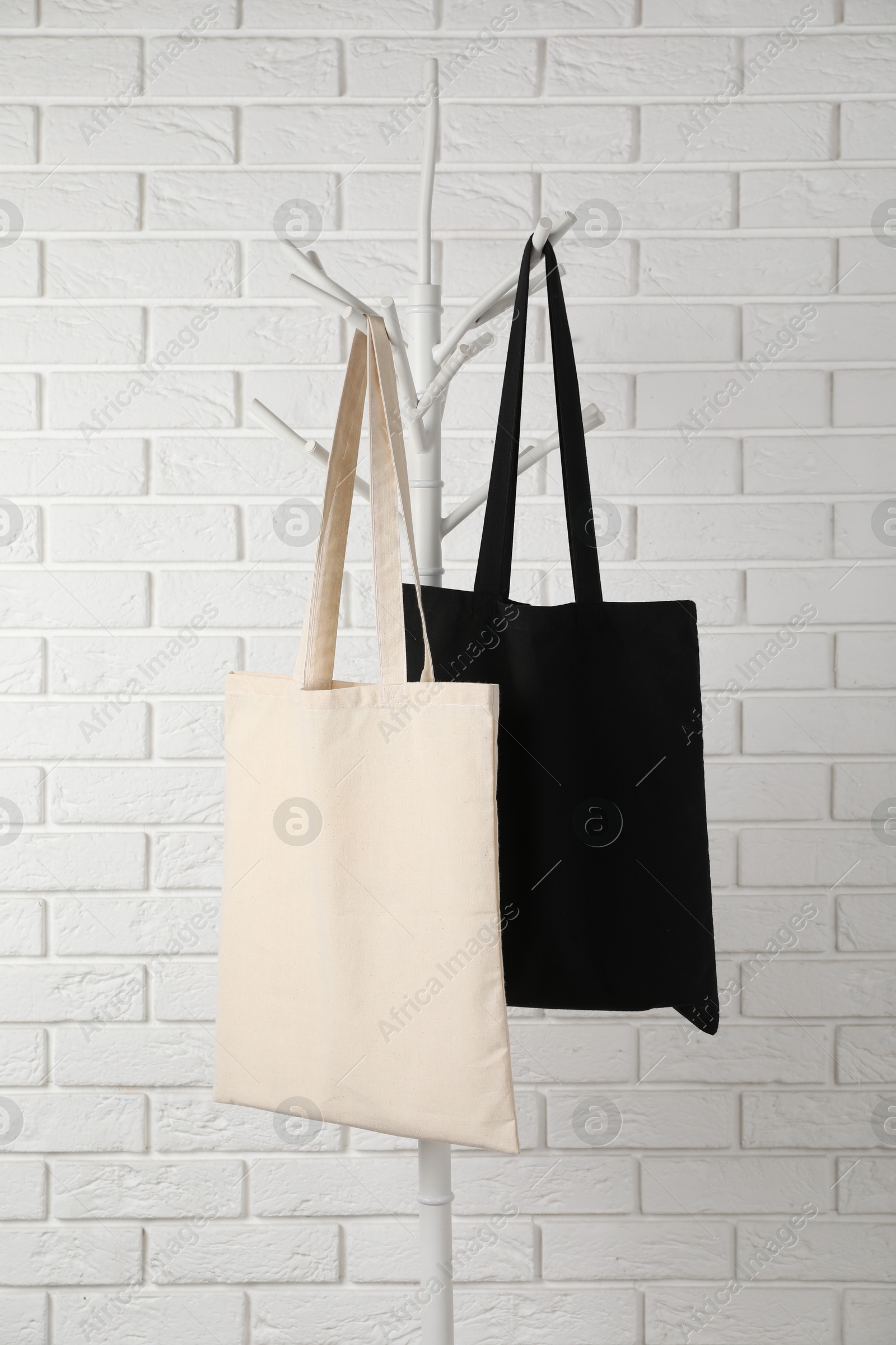 Photo of Eco bags hanging on clothing rack near white brick wall. Mockup for design