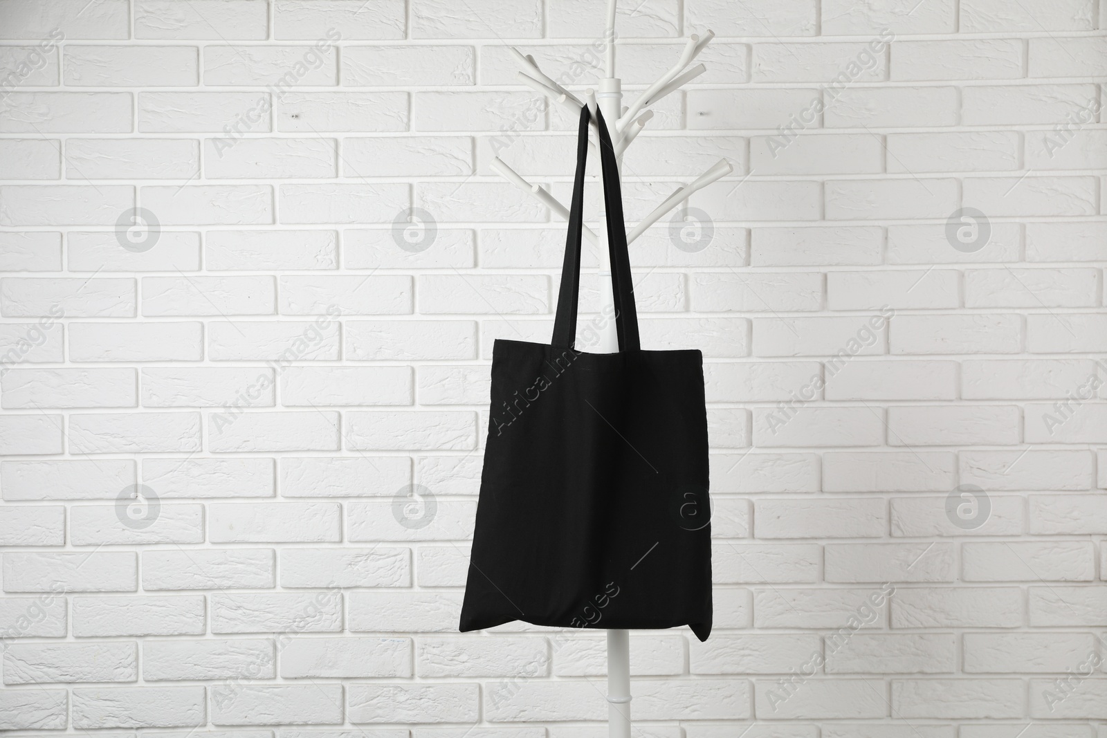 Photo of Black eco bag hanging on clothing rack near white brick wall. Mockup for design