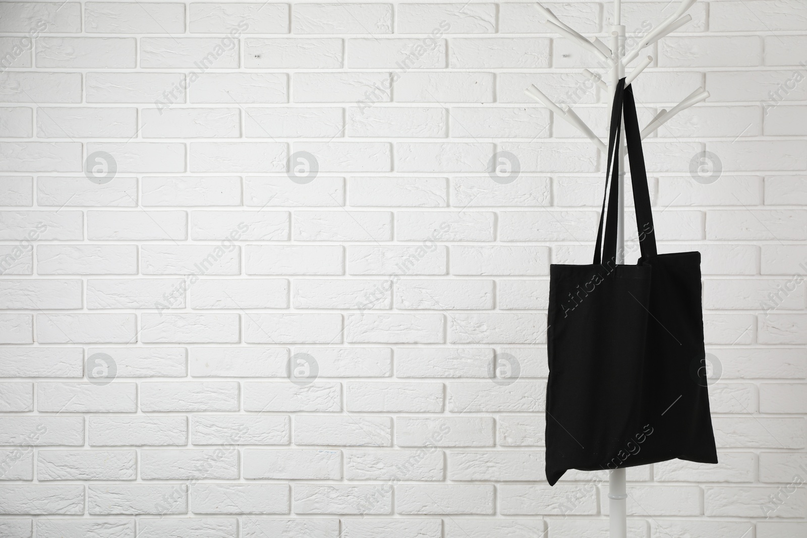 Photo of Black eco bag hanging on clothing rack near white brick wall. Mockup for design