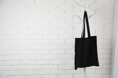 Photo of Black eco bag hanging on clothing rack near white brick wall. Mockup for design