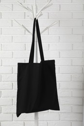 Photo of Black eco bag hanging on clothing rack near white brick wall. Mockup for design