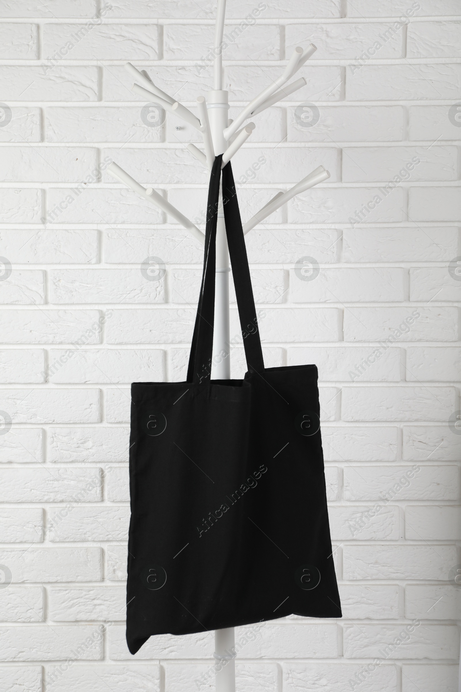 Photo of Black eco bag hanging on clothing rack near white brick wall. Mockup for design