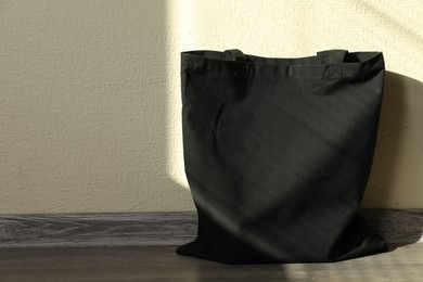 Photo of Black eco bag on floor near beige wall. Mockup for design