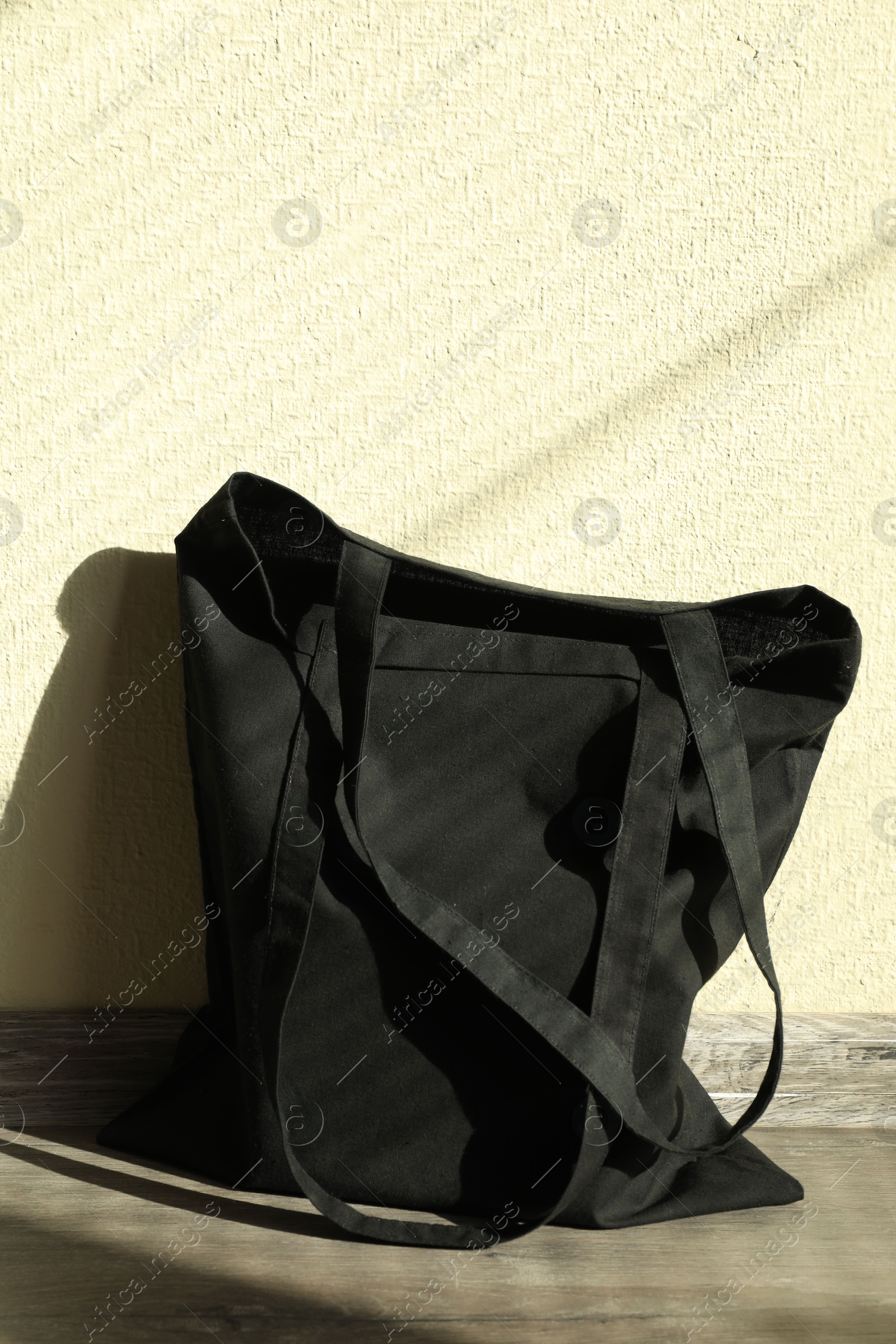 Photo of Black eco bag on floor near beige wall. Mockup for design