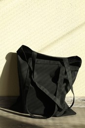 Photo of Black eco bag on floor near beige wall. Mockup for design