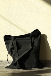 Photo of Black eco bag on floor near beige wall. Mockup for design