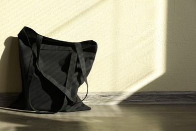 Photo of Black eco bag on floor near beige wall. Mockup for design