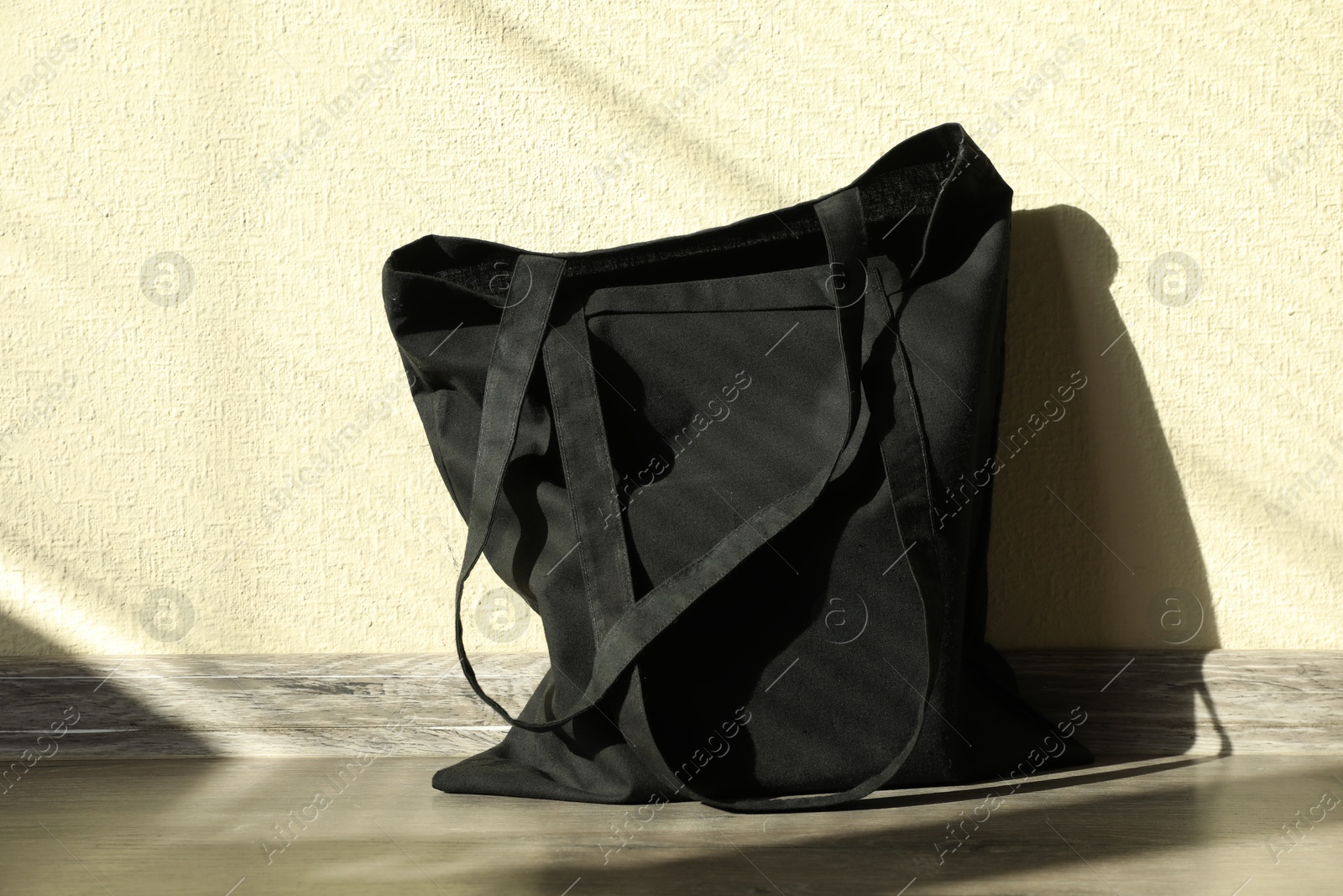 Photo of Black eco bag on floor near beige wall. Mockup for design