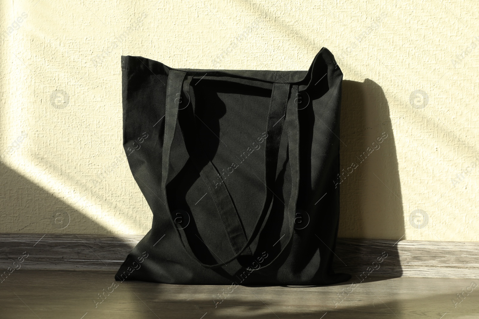 Photo of Black eco bag on floor near beige wall. Mockup for design