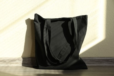 Photo of Black eco bag on floor near beige wall. Mockup for design