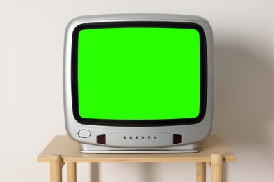 Image of Retro Tv set with green screen on wooden table near white wall. Chroma key