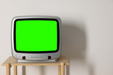 Image of Retro Tv set with green screen on wooden table near white wall, space for design. Chroma key