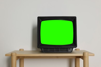 Image of Retro Tv set with green screen on wooden table near white wall, space for design. Chroma key