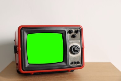 Image of Retro Tv set with green screen on wooden table near white wall, space for design. Chroma key