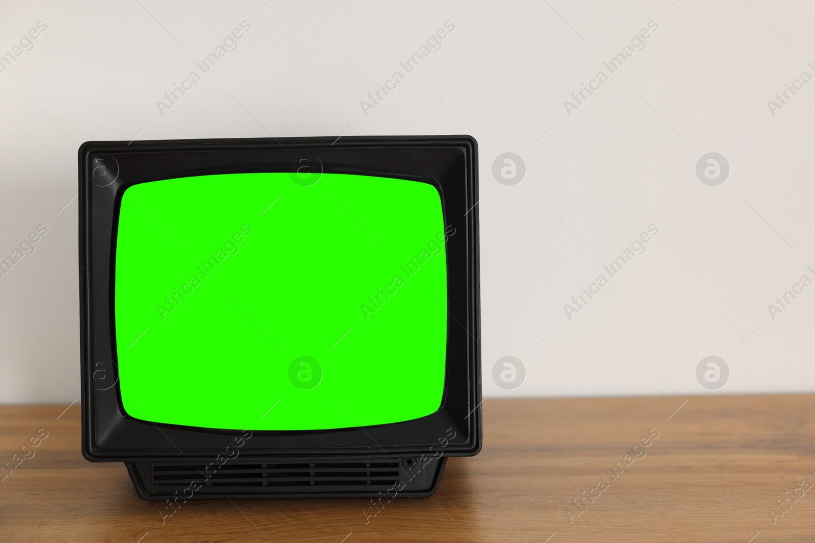 Image of Retro Tv set with green screen on wooden table near white wall, space for design. Chroma key