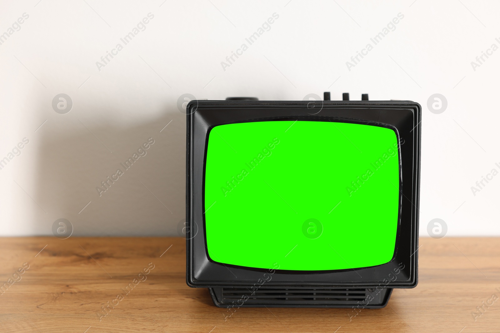 Image of Retro Tv set with green screen on wooden table near white wall, space for design. Chroma key