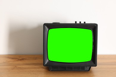 Image of Retro Tv set with green screen on wooden table near white wall, space for design. Chroma key