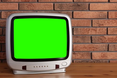 Image of Retro Tv set with green screen on wooden table near brick wall, space for design. Chroma key