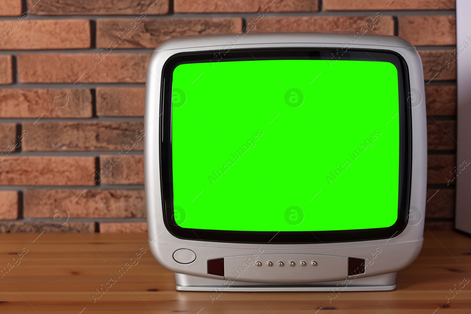 Image of Retro Tv set with green screen on wooden table near brick wall, space for design. Chroma key