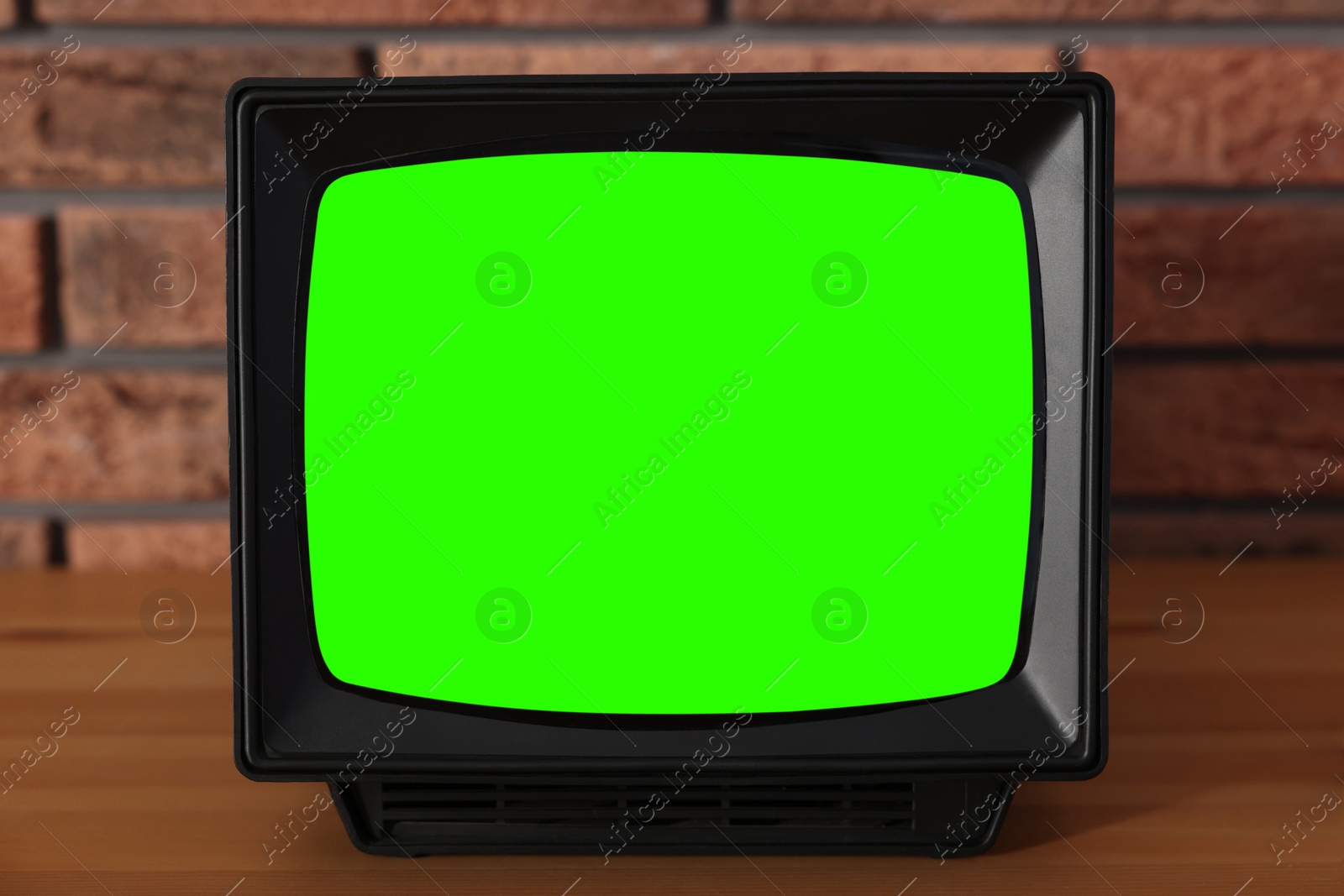 Image of Retro Tv set with green screen on wooden table near brick wall. Chroma key