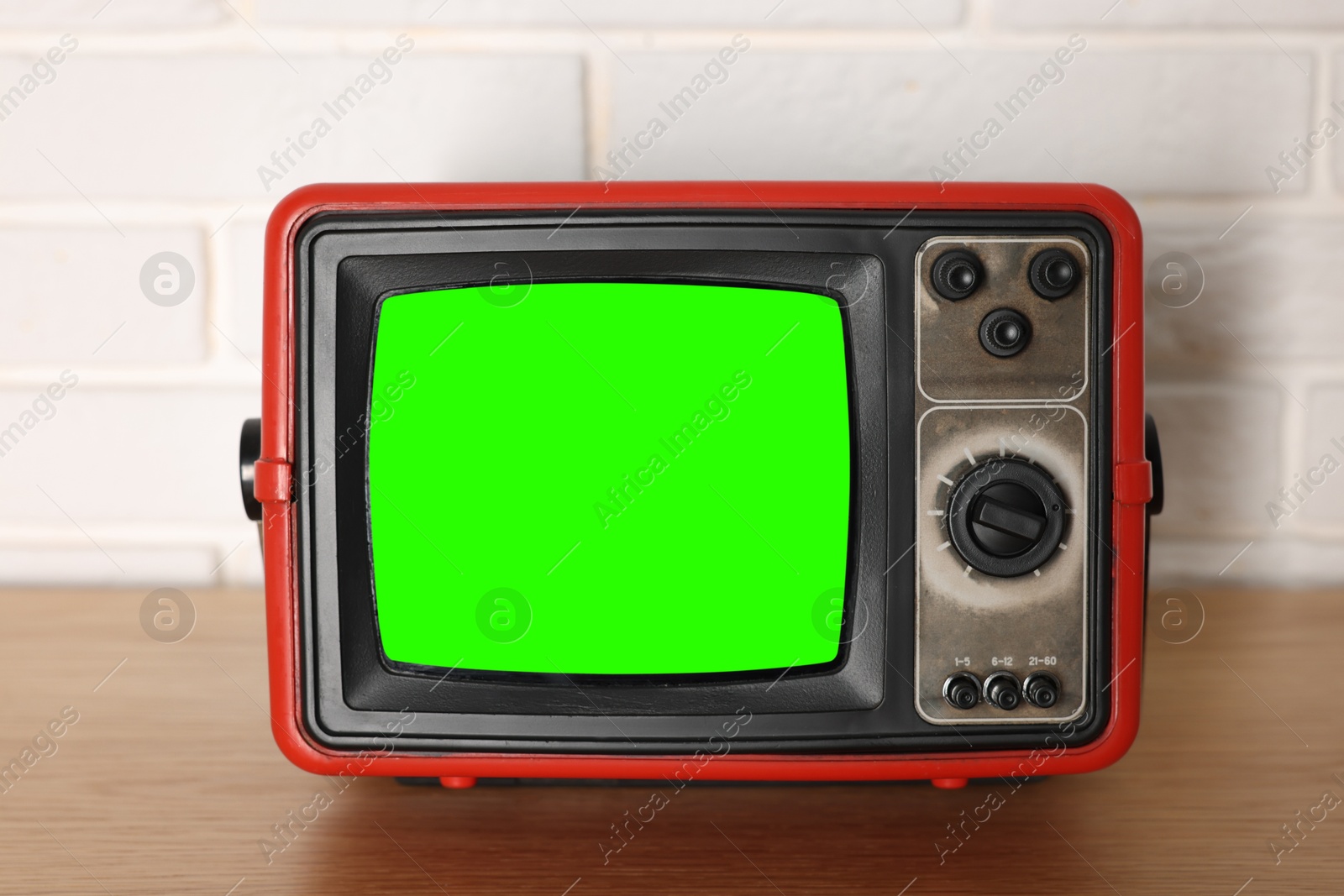 Image of Retro Tv set with green screen on wooden table near white brick wall. Chroma key