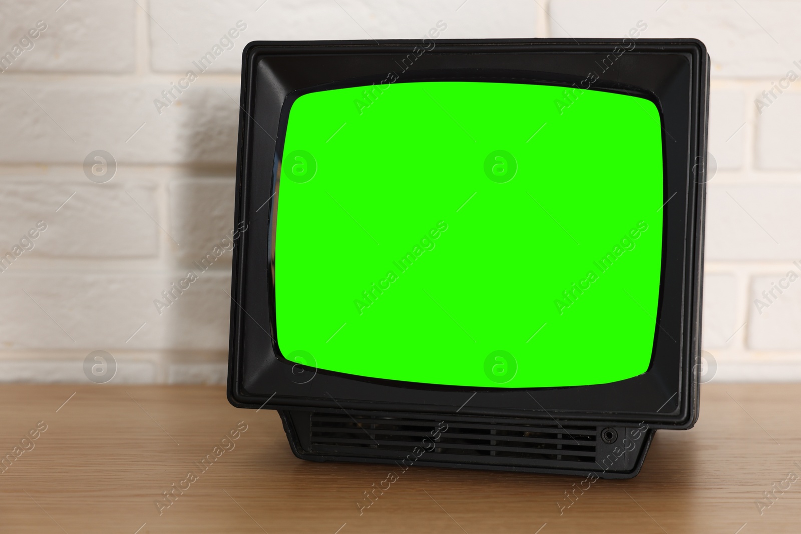 Image of Retro Tv set with green screen on wooden table near white brick wall, space for design. Chroma key