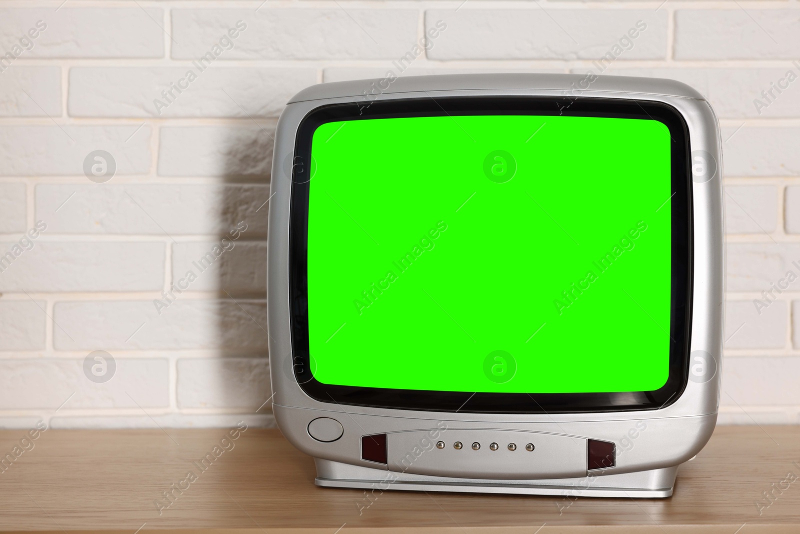 Image of Retro Tv set with green screen on wooden table near white brick wall, space for design. Chroma key